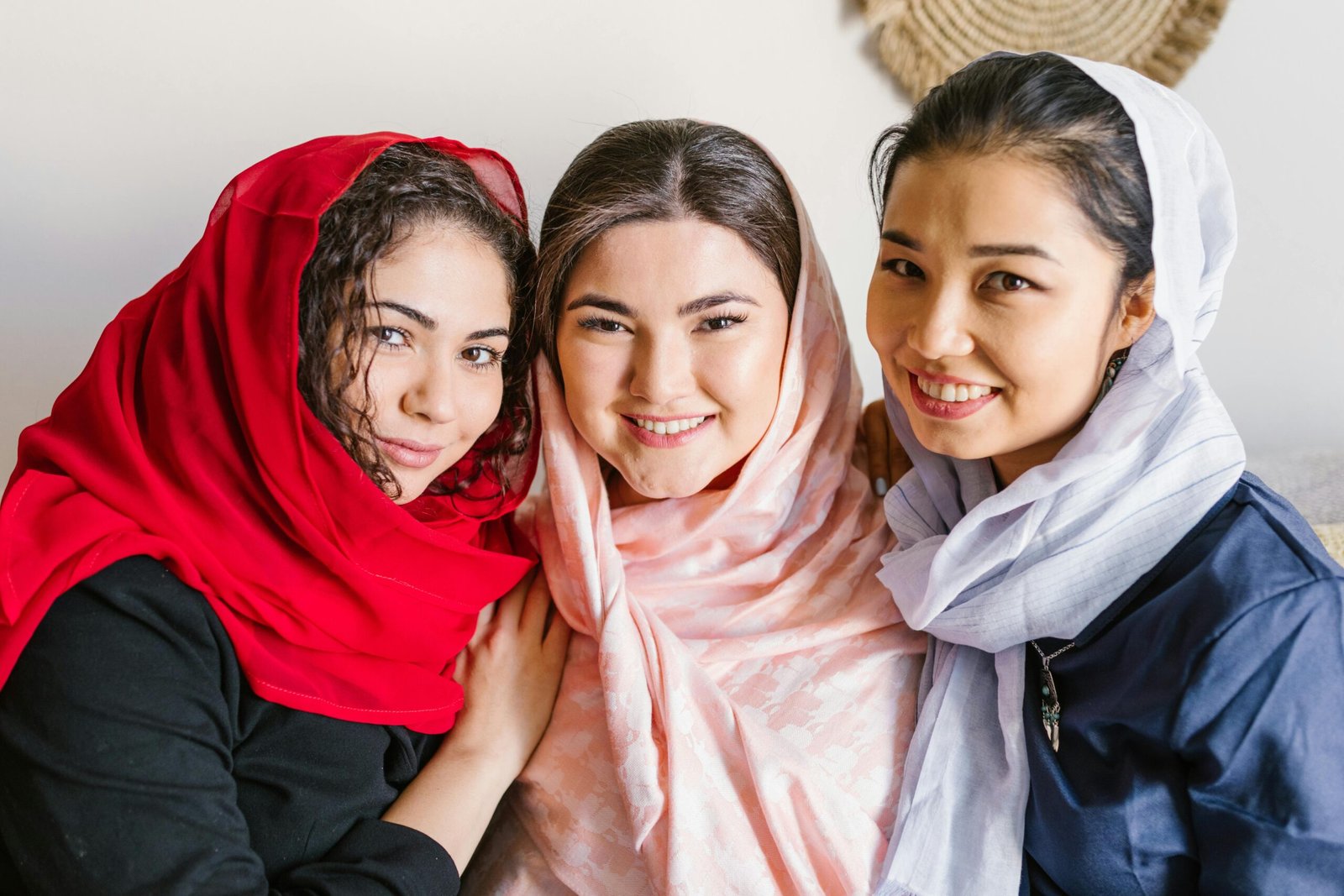 Three women smiling joyfully indoors, celebrating together with traditional headscarves.
